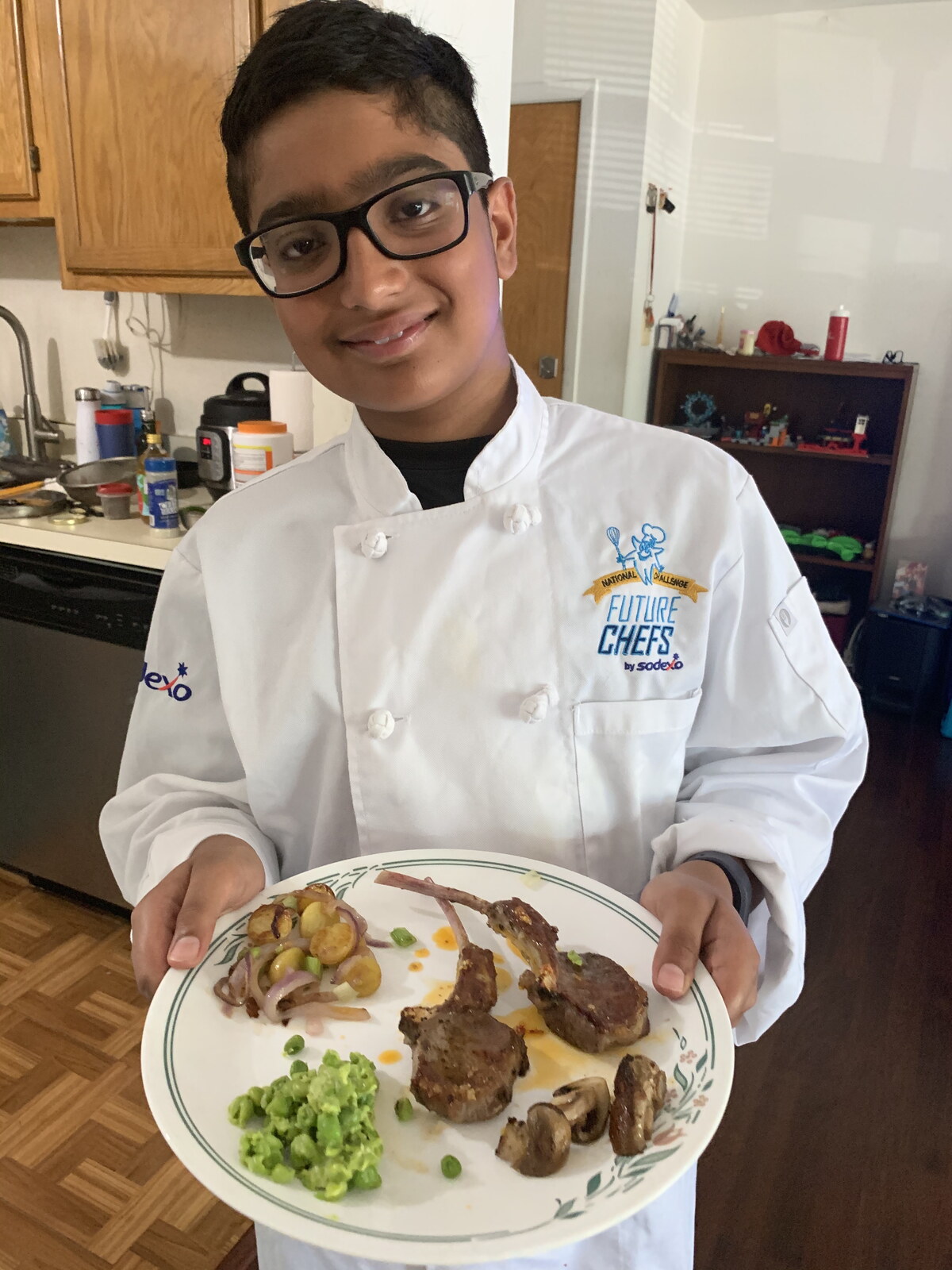 young me in a chef coat with a plate of lamb chops I made for my family